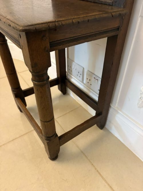 fig 3. A dark oak 17th-century correction chair featuring a tall panelled backrest, carved crest rail with small wooden finials, solid wooden seat, turned front legs, and plain stretchers.