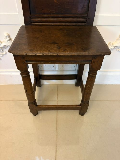 fig 4. A dark oak 17th-century correction chair featuring a tall panelled backrest, carved crest rail with small wooden finials, solid wooden seat, turned front legs, and plain stretchers.