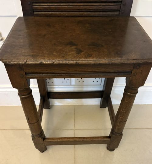fig 5. A dark oak 17th-century correction chair featuring a tall panelled backrest, carved crest rail with small wooden finials, solid wooden seat, turned front legs, and plain stretchers.