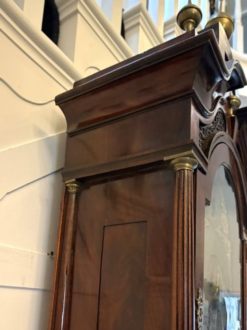 fig 5. An antique Georgian longcase grandfather clock crafted from flame mahogany wood with an arched brass dial and brass finials.