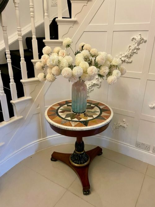 fig 1. A circular Victorian centre table featuring a geometric specimen marble inlaid top resting on a dark carved mahogany pedestal with a triform base.