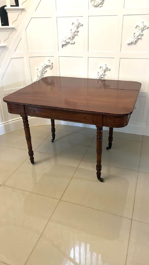 An antique George III mahogany console table featuring a polished rectangular top with rounded corners, a panelled frieze, and turned legs on brass castors. View II