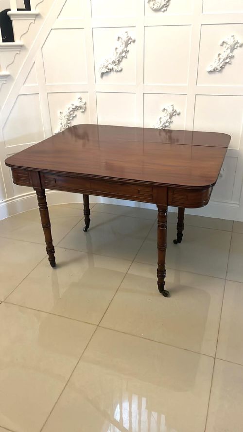 An antique George III mahogany console table featuring a polished rectangular top with rounded corners, a panelled frieze, and turned legs on brass castors. View V