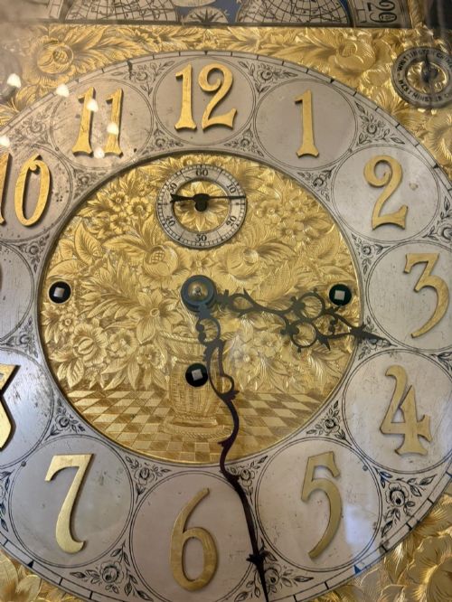 fig 4. A tall carved dark mahogany longcase clock featuring an ornate pediment, brass dial with moon phase indicator, and a glazed door displaying nine tubular chimes.