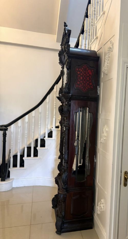 A tall carved dark mahogany longcase clock featuring an ornate pediment, brass dial with moon phase indicator, and a glazed door displaying nine tubular chimes. View XII