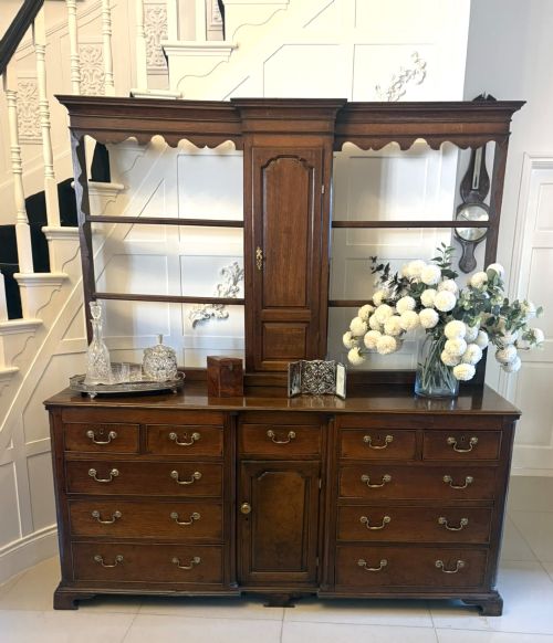 fig 5. A dark oak Georgian Lancashire dresser with a scalloped open plate rack, central cupboard section, and base containing multiple drawers with brass handles.
