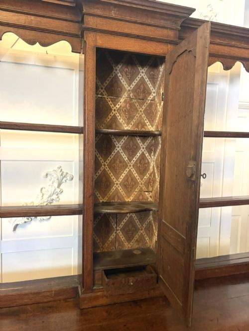 fig 7. A dark oak Georgian Lancashire dresser with a scalloped open plate rack, central cupboard section, and base containing multiple drawers with brass handles.