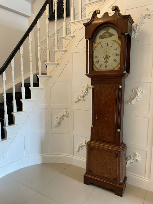 fig 1. An antique George III oak longcase clock featuring a swan-neck pediment, brass fittings, and a painted arch dial with Roman numerals.