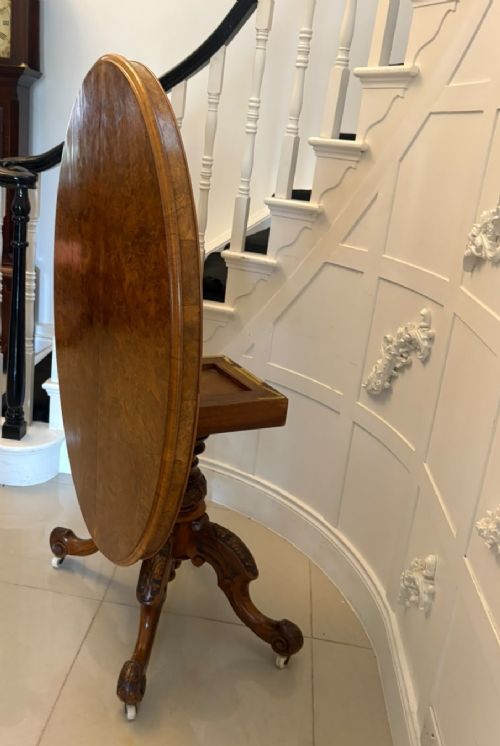 An antique Victorian oval tilt-top table made of burr walnut with a four-star carved pedestal base and white ceramic castors, shown with the tabletop tilted vertically. View XIV