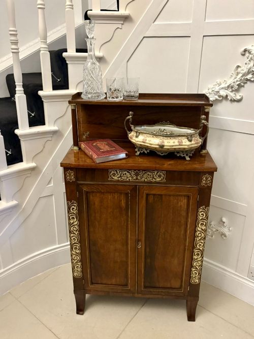 fig 3. An antique Regency mahogany chiffonier cabinet featuring brass foliate inlay, a raised upper shelf supported by turned brass-capped pillars, and two panelled cupboard doors.