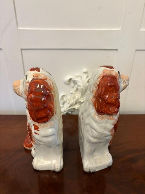 fig 1. A pair of Victorian Staffordshire ceramic spaniel figurines with painted russet spots and black chain collars seated on a dark wooden surface.