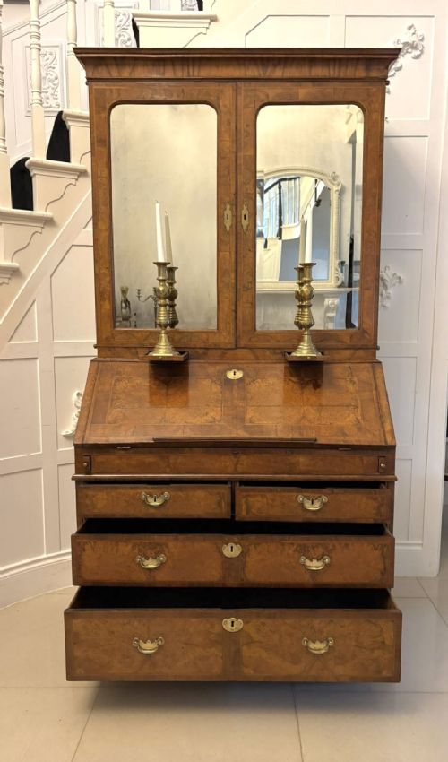 fig 5. An 18th-century George I figured walnut bureau bookcase featuring two mirrored upper cabinet doors, a slant-front writing desk, and three lower drawers on bracket feet.