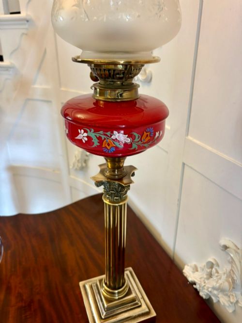 fig 1. An antique Victorian oil lamp featuring a stepped square brass base, a fluted Corinthian column stem, an enamel-painted red glass font, and an etched cranberry glass frilled shade.