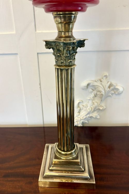 fig 2. An antique Victorian oil lamp featuring a stepped square brass base, a fluted Corinthian column stem, an enamel-painted red glass font, and an etched cranberry glass frilled shade.