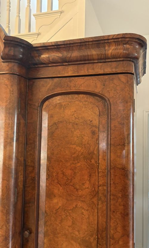 An antique Victorian burr walnut three-door wardrobe featuring an arched central mirrored door crowned with a carved crest, flanked by two burr walnut panelled doors. View II