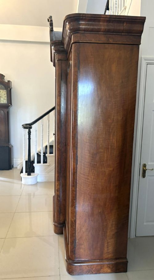 An antique Victorian burr walnut three-door wardrobe featuring an arched central mirrored door crowned with a carved crest, flanked by two burr walnut panelled doors. View VI