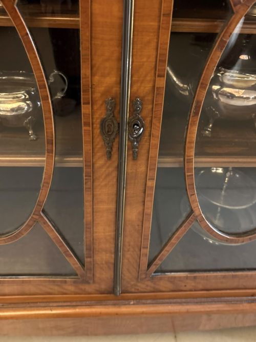 fig 3. A Georgian Sheraton style satinwood display cabinet featuring upper open shelves with brass grilles and marquetry panels, positioned above a lower glazed twin-door cabinet with oval astragal bars.