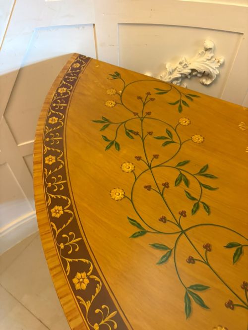 fig 6. A semicircular satinwood demi-lune cabinet featuring hand-painted neoclassical leaf swags, a central figural medallion, and short tapered feet.