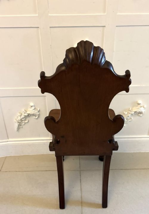 A pair of Victorian carved mahogany hall chairs with shaped timber seats, scrolled cartouche backrests, and carved cabriole legs. View IV