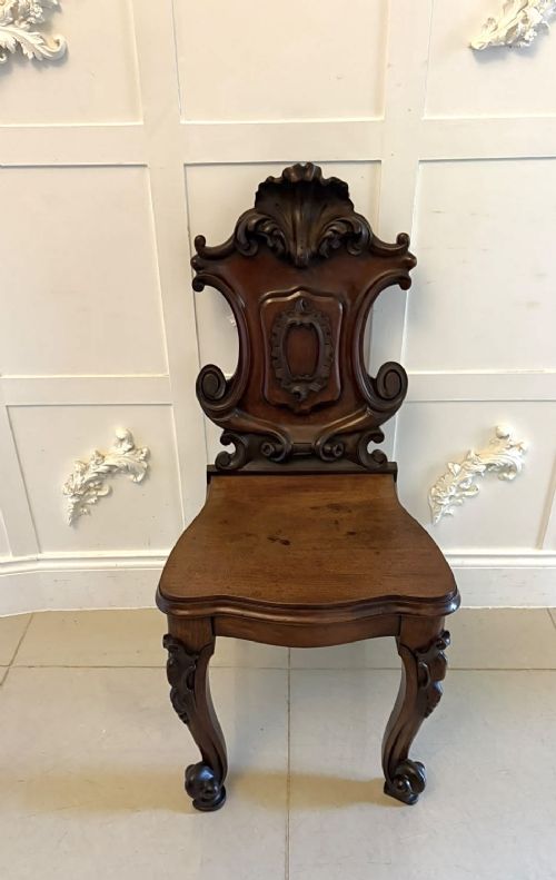 A pair of Victorian carved mahogany hall chairs with shaped timber seats, scrolled cartouche backrests, and carved cabriole legs. View IX