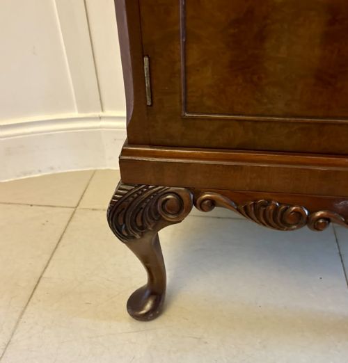 fig 2. An antique burr walnut cocktail cabinet featuring decorative brass hardware, carved scroll cresting, two cupboard sections, and cabriole legs.