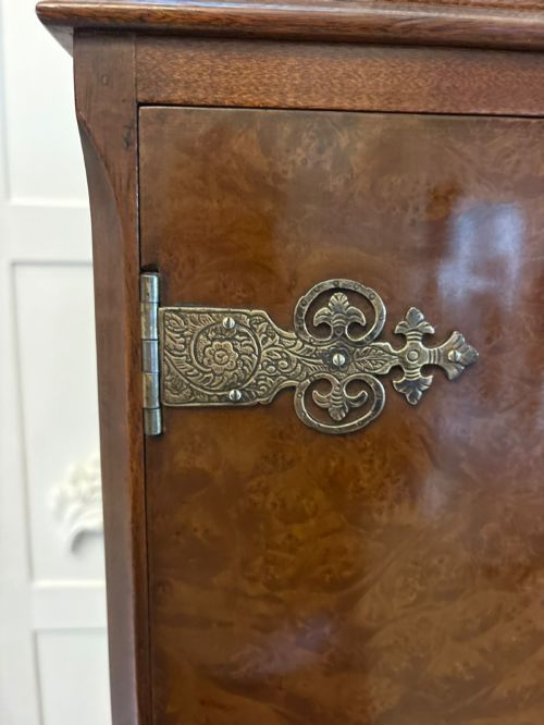 fig 4. An antique burr walnut cocktail cabinet featuring decorative brass hardware, carved scroll cresting, two cupboard sections, and cabriole legs.