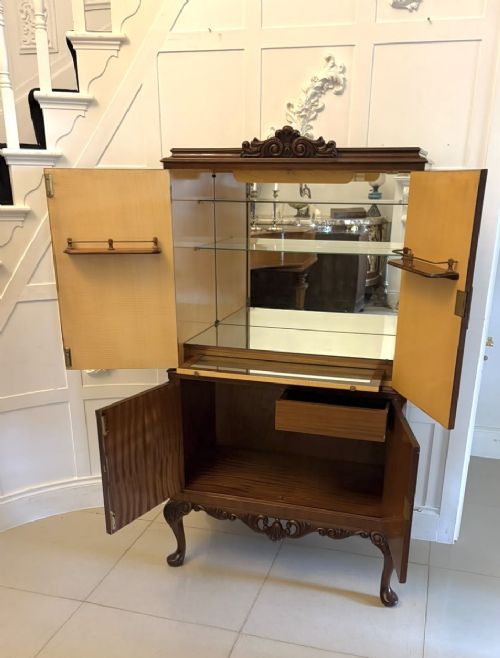 An antique burr walnut cocktail cabinet featuring decorative brass hardware, carved scroll cresting, two cupboard sections, and cabriole legs. View VII