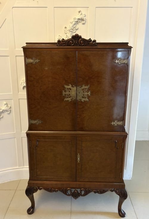 An antique burr walnut cocktail cabinet featuring decorative brass hardware, carved scroll cresting, two cupboard sections, and cabriole legs. View IX