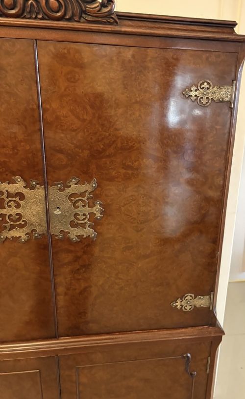An antique burr walnut cocktail cabinet featuring decorative brass hardware, carved scroll cresting, two cupboard sections, and cabriole legs. View XI