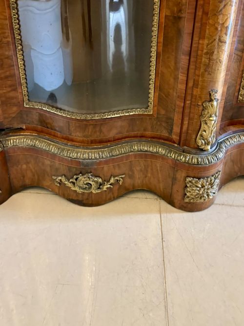 fig 5. A Victorian serpentine burr walnut credenza featuring detailed floral marquetry inlays, gilt-bronze mounts, a central panelled door, and two curved glazed side doors.