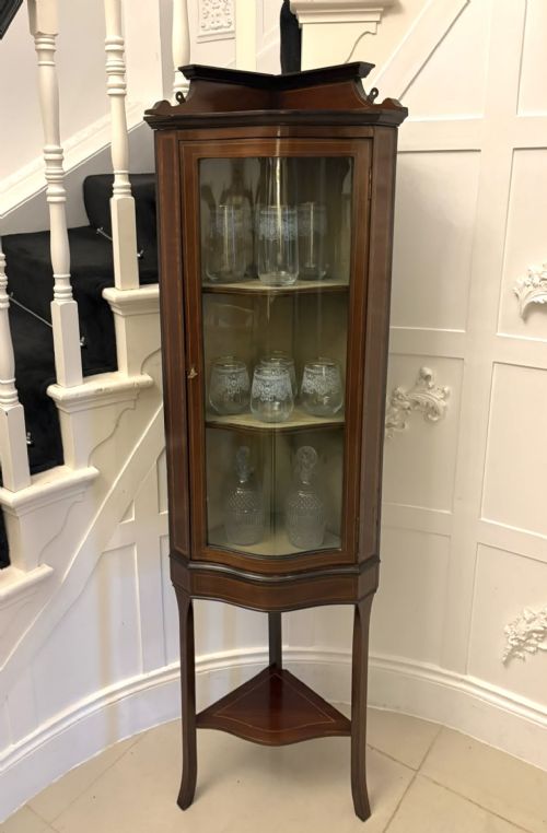 fig 1. An Edwardian mahogany corner display cabinet with a serpentine glazed door, line inlay decoration, shaped upper pediment, and slender tapered legs with a lower undertier.