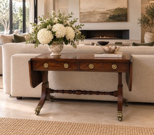 fig 1. A Regency mahogany sofa table featuring two drop leaves, two front drawers with round brass knobs, reeded splayed legs, and brass paw castors.