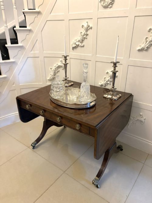 fig 2. A Regency mahogany sofa table featuring two drop leaves, two front drawers with round brass knobs, reeded splayed legs, and brass paw castors.