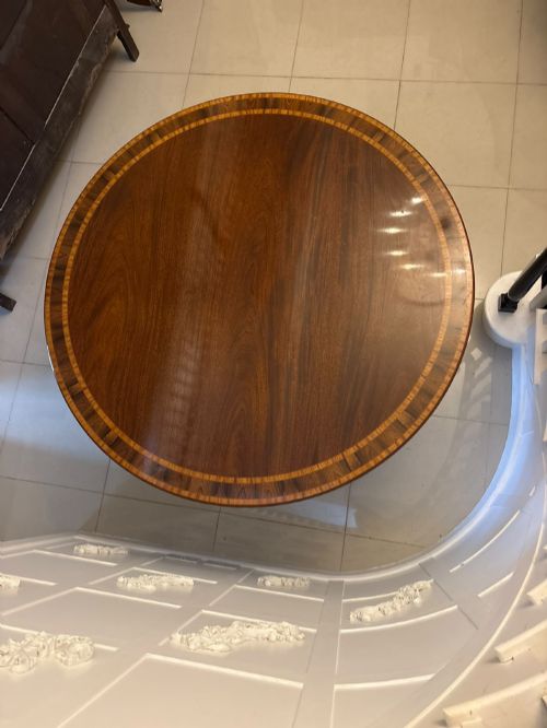 fig 1. A large circular mahogany dining table featuring rosewood and satinwood crossbanding set upon a central pedestal base with reeded legs ending in brass castors.