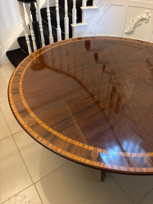 fig 4. A large circular mahogany dining table featuring rosewood and satinwood crossbanding set upon a central pedestal base with reeded legs ending in brass castors.