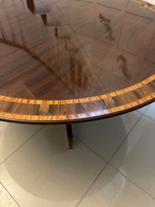 fig 5. A large circular mahogany dining table featuring rosewood and satinwood crossbanding set upon a central pedestal base with reeded legs ending in brass castors.