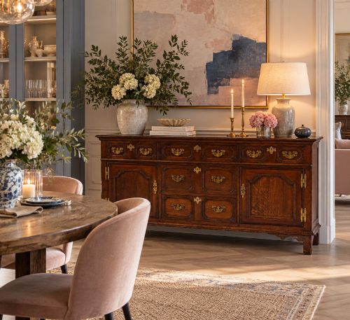 fig 1. An antique dark oak Georgian dresser base featuring geometric panel drawers, brass handles, side cupboard doors, and a smooth wooden surface.