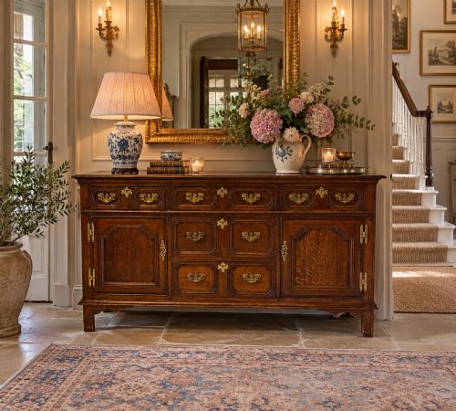 fig 2. An antique dark oak Georgian dresser base featuring geometric panel drawers, brass handles, side cupboard doors, and a smooth wooden surface.