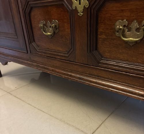 fig 5. An antique dark oak Georgian dresser base featuring geometric panel drawers, brass handles, side cupboard doors, and a smooth wooden surface.