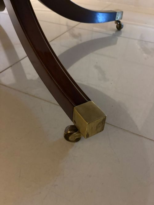fig 3. A circular mahogany dining table with a crossbanded edge tilted vertically on a central pedestal base with splayed legs and brass castors.