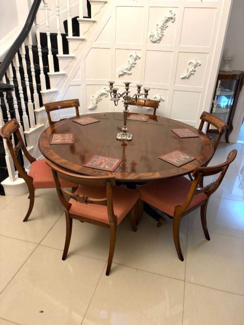 fig 4. A circular mahogany dining table with a crossbanded edge tilted vertically on a central pedestal base with splayed legs and brass castors.