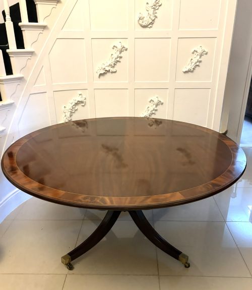 fig 5. A circular mahogany dining table with a crossbanded edge tilted vertically on a central pedestal base with splayed legs and brass castors.