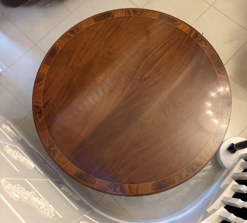 fig 6. A circular mahogany dining table with a crossbanded edge tilted vertically on a central pedestal base with splayed legs and brass castors.