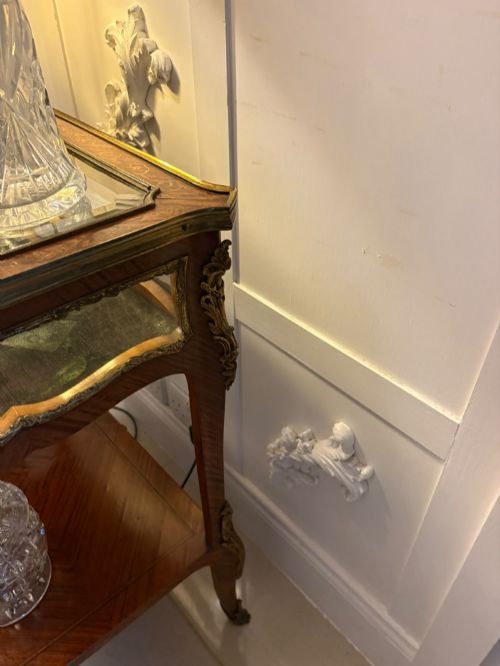 fig 4. An antique French Napoleon III satinwood bijouterie table featuring a glazed display top, curved cabriole legs with decorative brass mounts, and an undertier shelf.