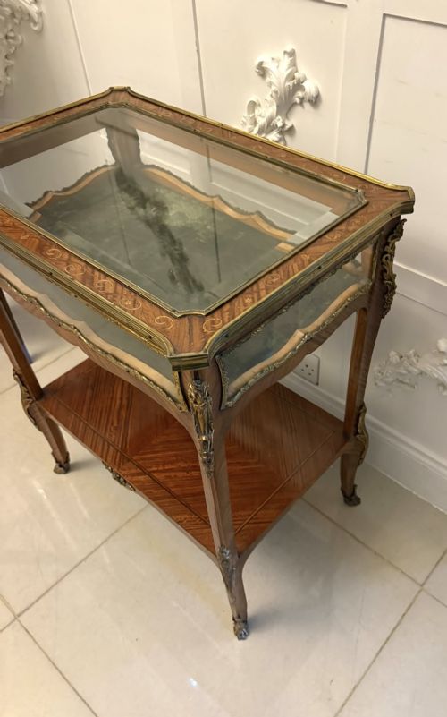 An antique French Napoleon III satinwood bijouterie table featuring a glazed display top, curved cabriole legs with decorative brass mounts, and an undertier shelf. View XII
