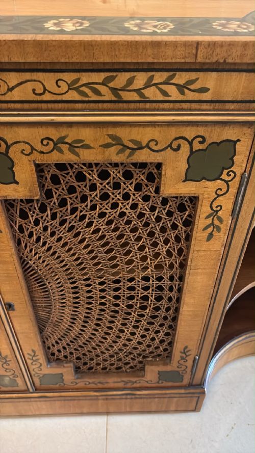 fig 2. A Sheraton Revival satinwood side cabinet featuring painted leaf borders, central doors with fan-shaped woven cane panels, and open curved side shelves.