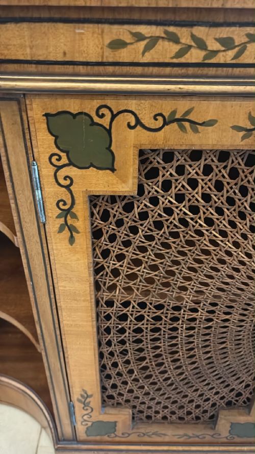 fig 3. A Sheraton Revival satinwood side cabinet featuring painted leaf borders, central doors with fan-shaped woven cane panels, and open curved side shelves.