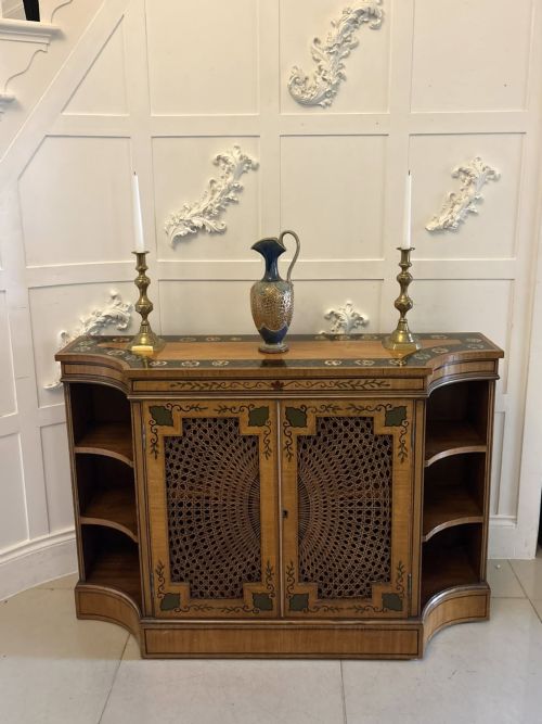 fig 4. A Sheraton Revival satinwood side cabinet featuring painted leaf borders, central doors with fan-shaped woven cane panels, and open curved side shelves.