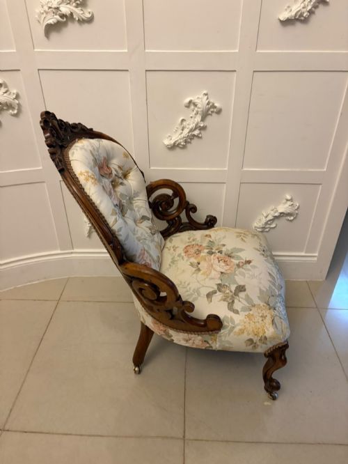 fig 3. A Victorian walnut armchair featuring floral button-tufted upholstery, carved open scroll arms, and front legs set on brass castors.