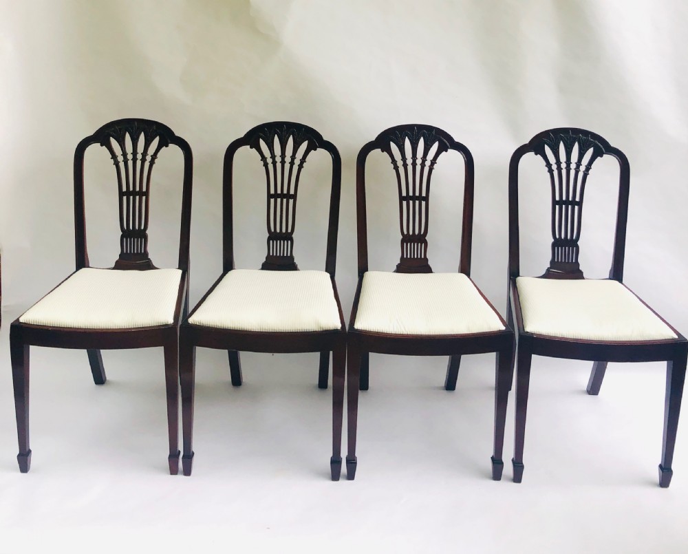 A set of four dark mahogany dining chairs featuring carved fan splats, cream upholstered seats, and tapered legs.